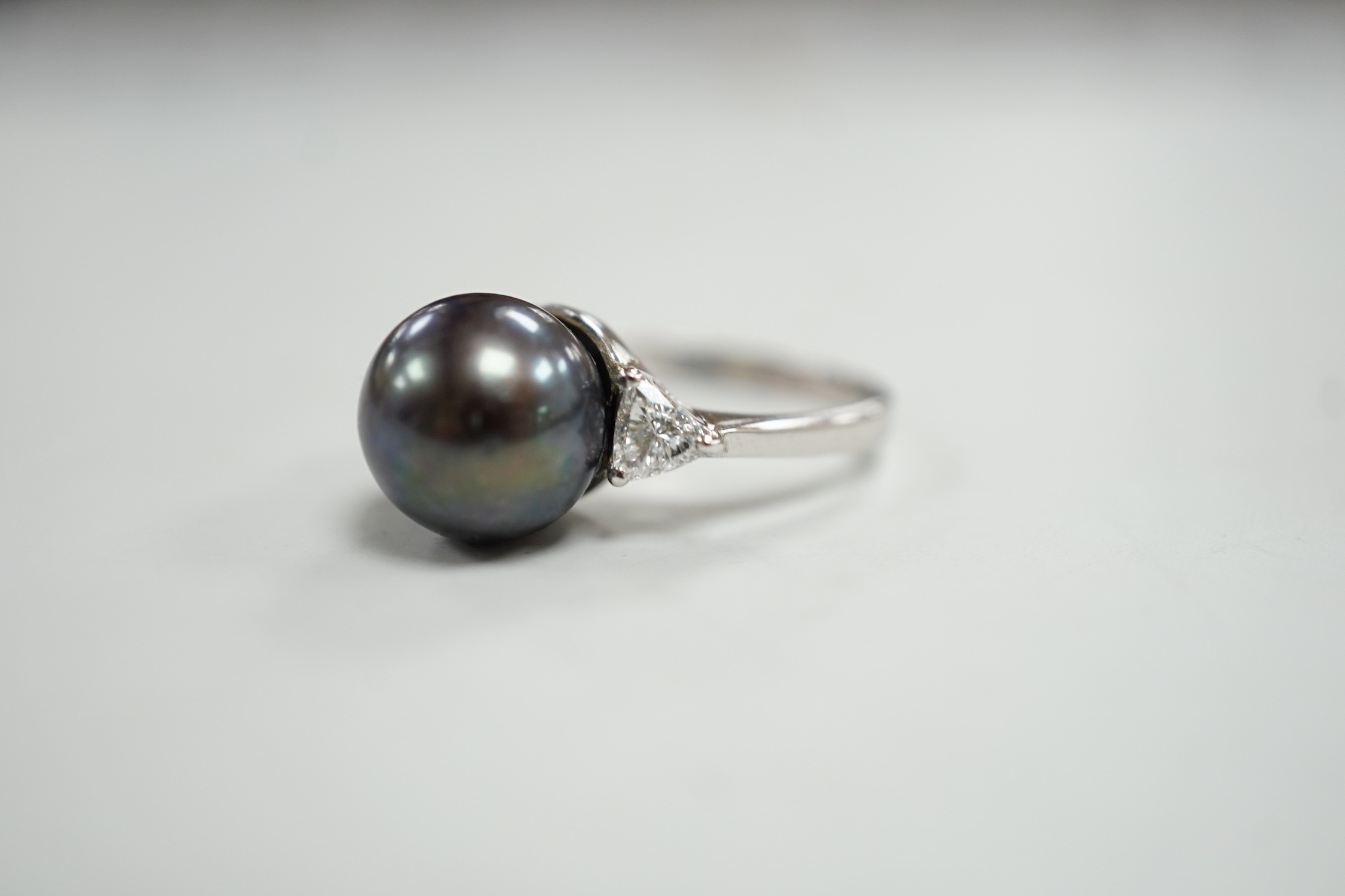 A modern 750 white metal, single stone Tahitian pearl and two stone trillion cut diamond set ring, size O, gross weight 5.6 grams.